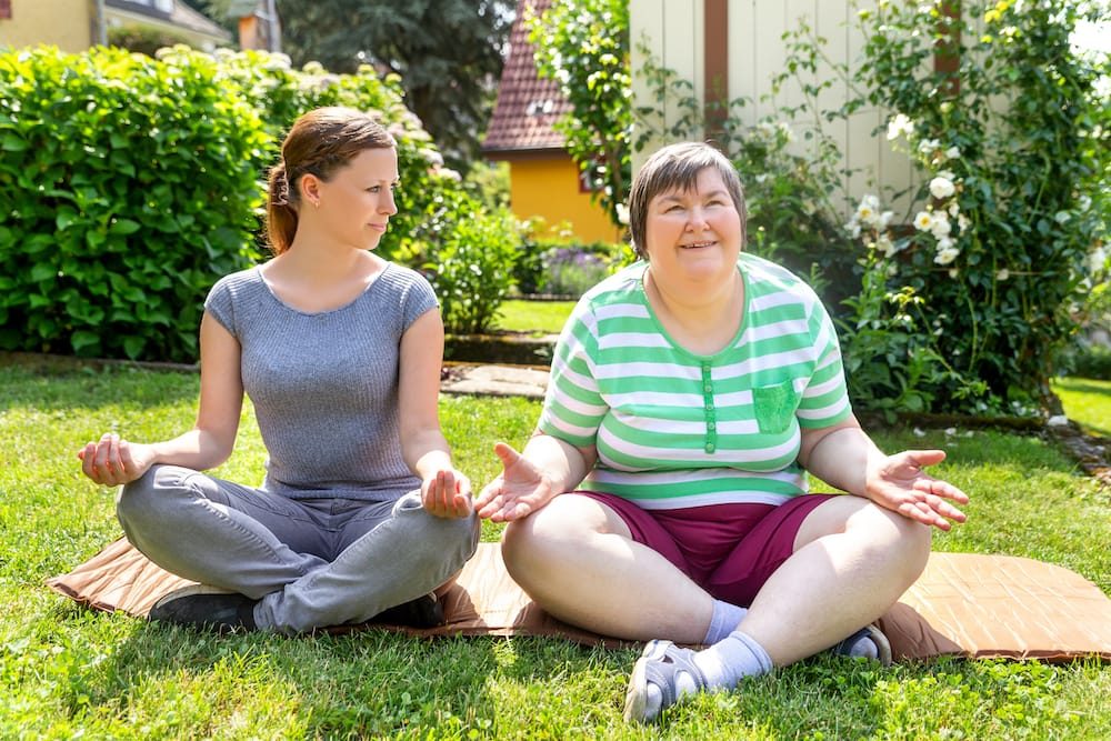 An old lady doing yoga on the garden with a young lady