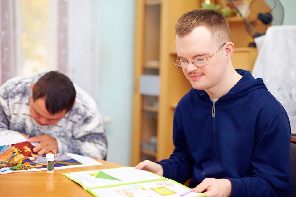 Two down syndrome men are reading books.
